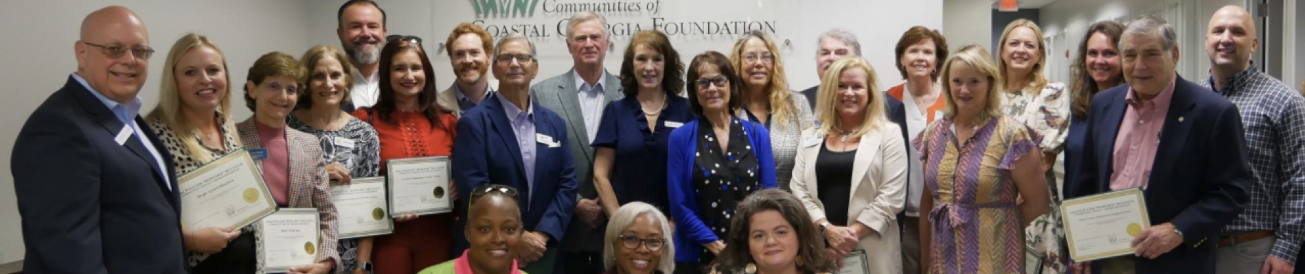 Group of award recipients smiling, holding certificates indoors.